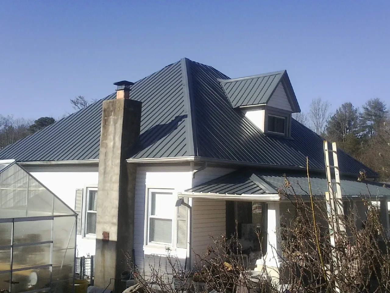 Dark blue standing seam metal roof on a white farmhouse with dormer — Slate & Tile Roof Repair by Roofing Brothers in Meadowview