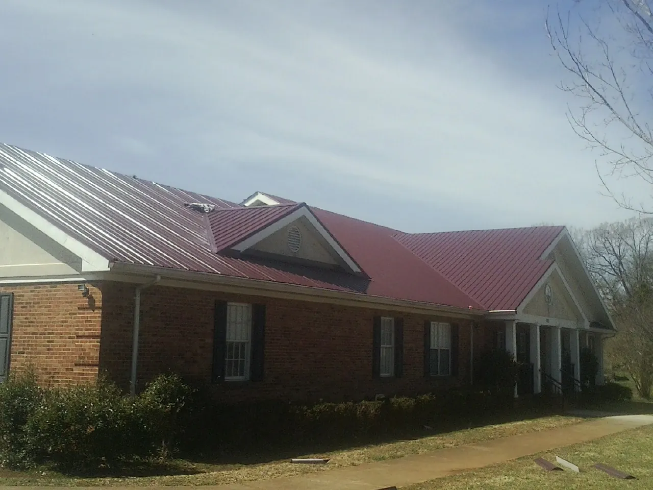 Red metal roof with gabled entries on a long brick building, from a Hail Damage Roof Repair job in Meadowview