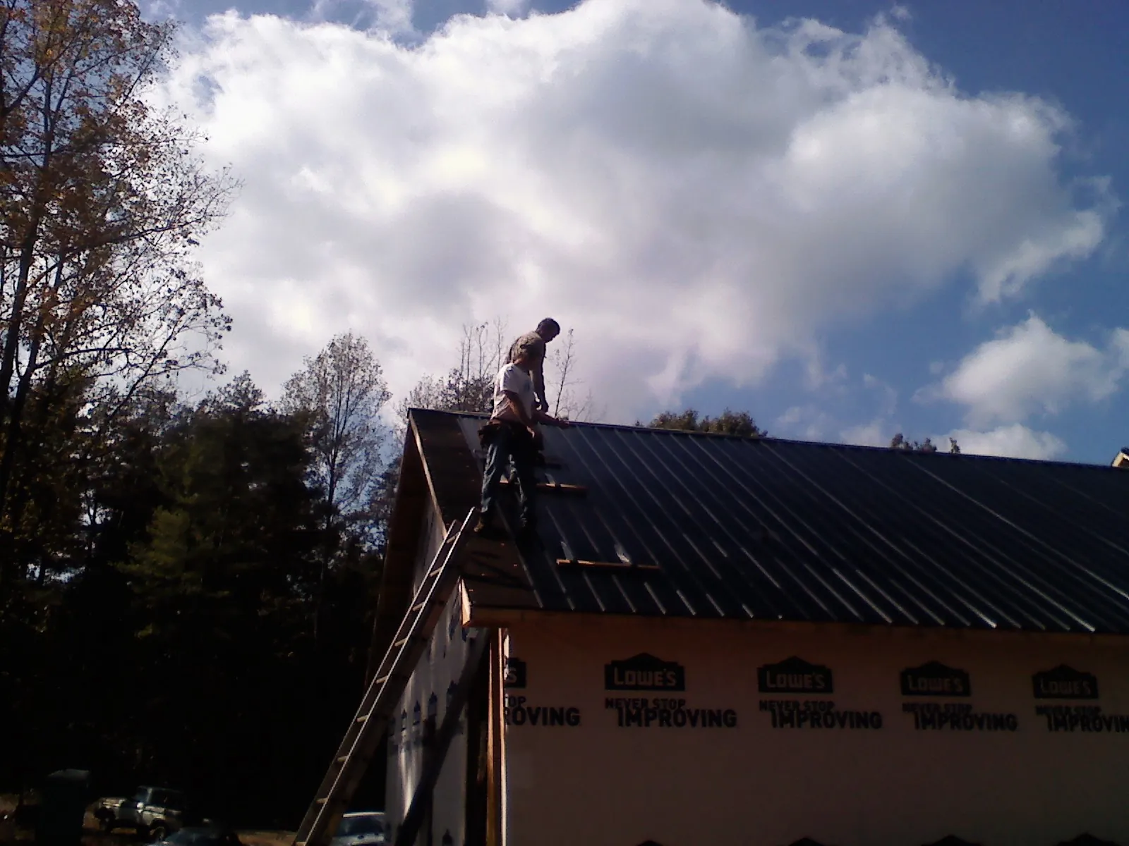 Roofer fastening dark metal panels high against a cloudy sky, from a Roof Inspection job in Meadowview